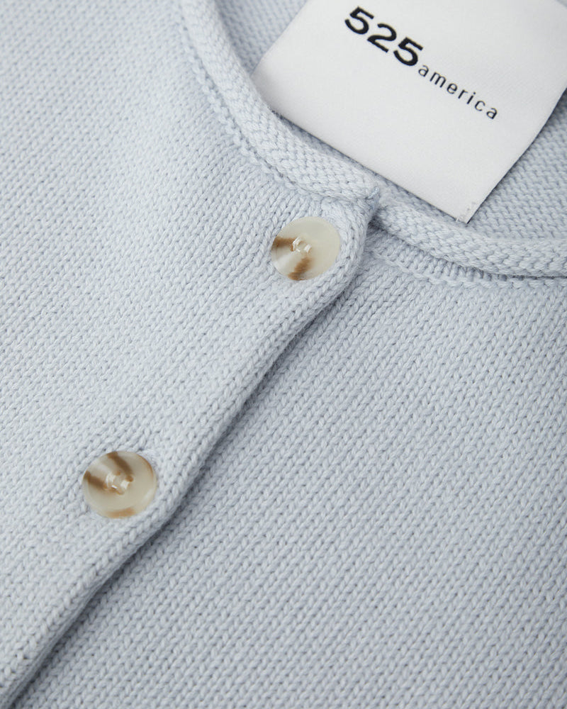 Close-up of a light gray sweater with buttons and a brand label.