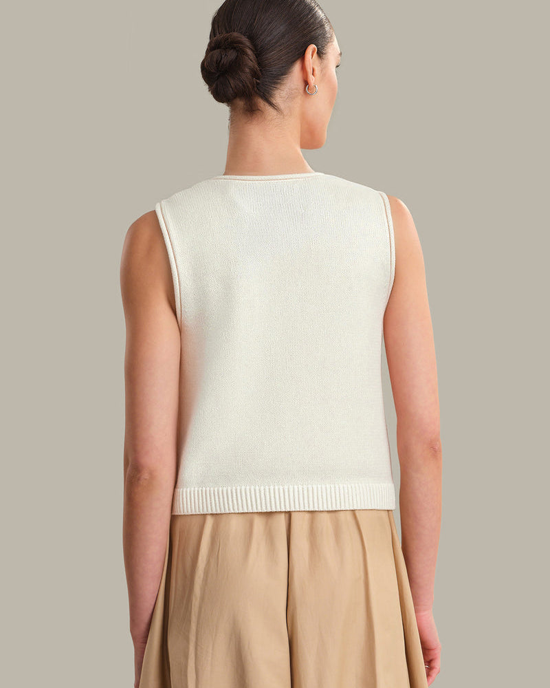 Woman wearing a cream sleeveless sweater vest against a neutral background