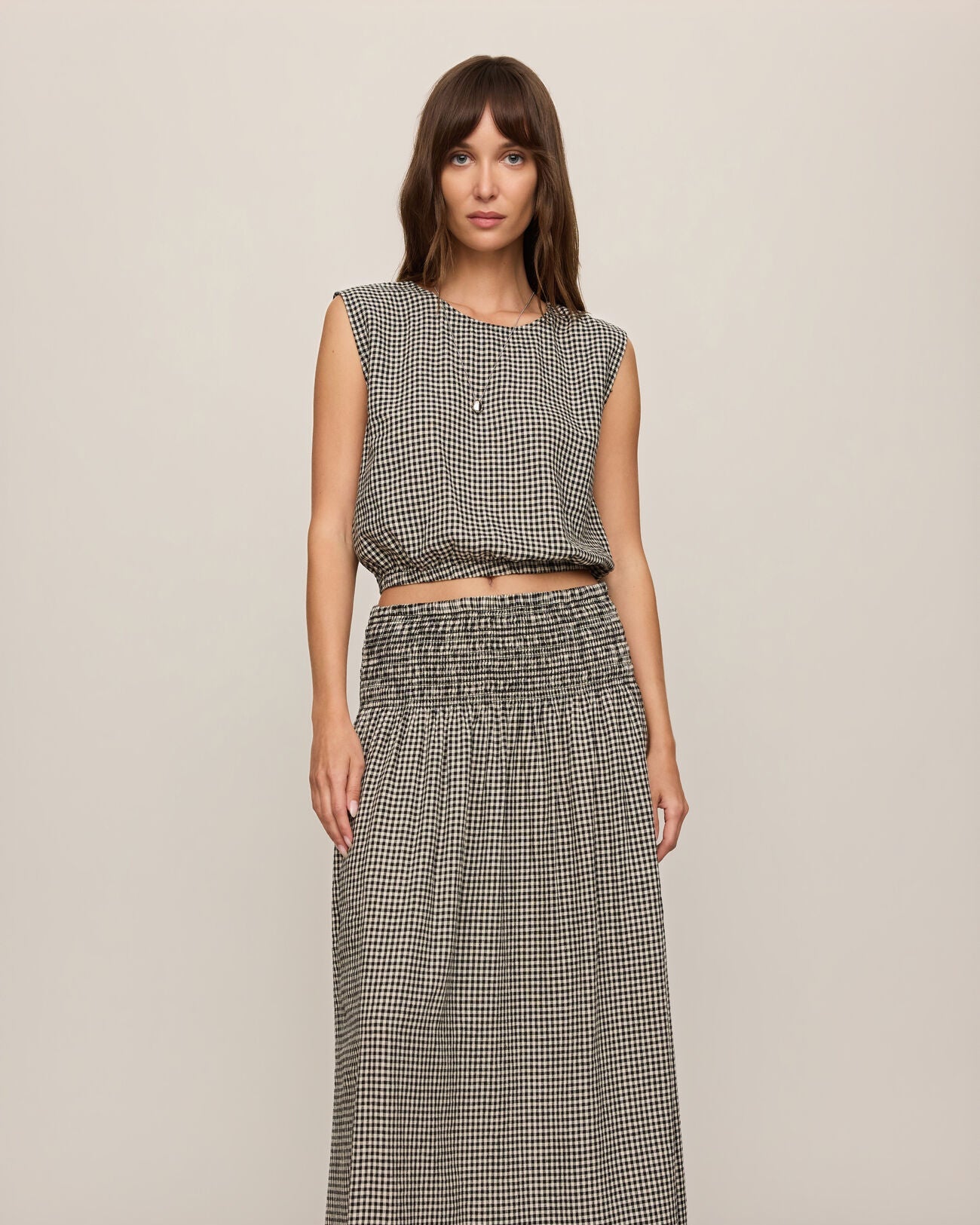 Woman wearing a checkered sleeveless top and long skirt on a beige background