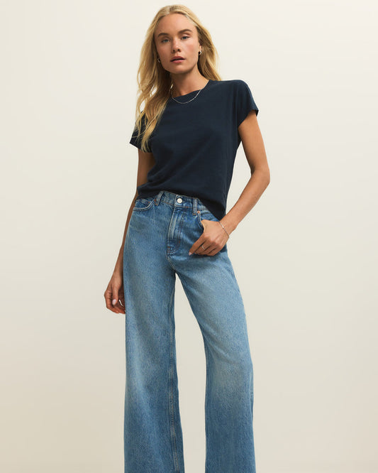 Woman wearing a navy t-shirt and blue jeans on a plain background