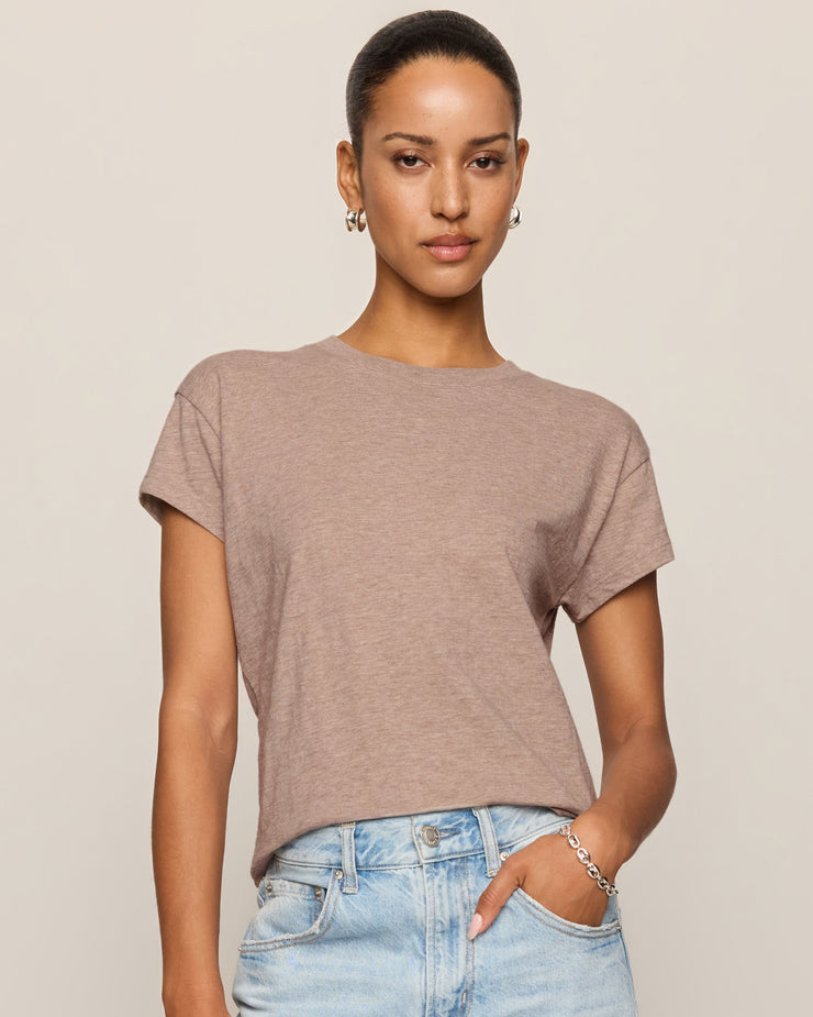 Woman wearing a brown t-shirt and light blue jeans against a beige background