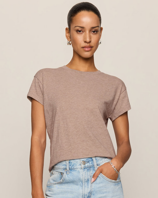 Woman wearing a brown t-shirt and light blue jeans against a beige background