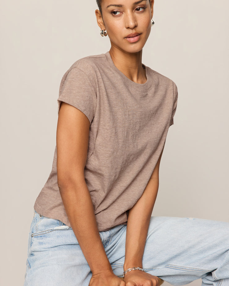Woman wearing a brown t-shirt and light blue jeans against a beige background