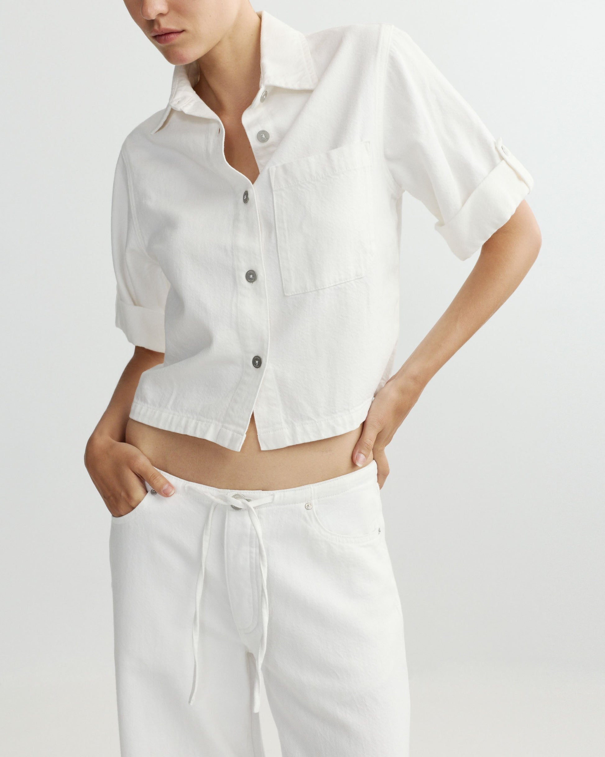 Person wearing a white button-up shirt and pants on a light gray background