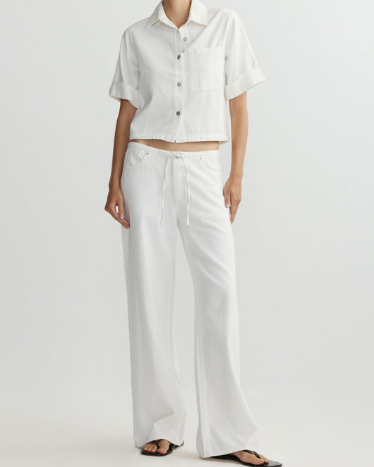 Person wearing a white outfit with a short-sleeve shirt and wide-leg pants on a light gray background