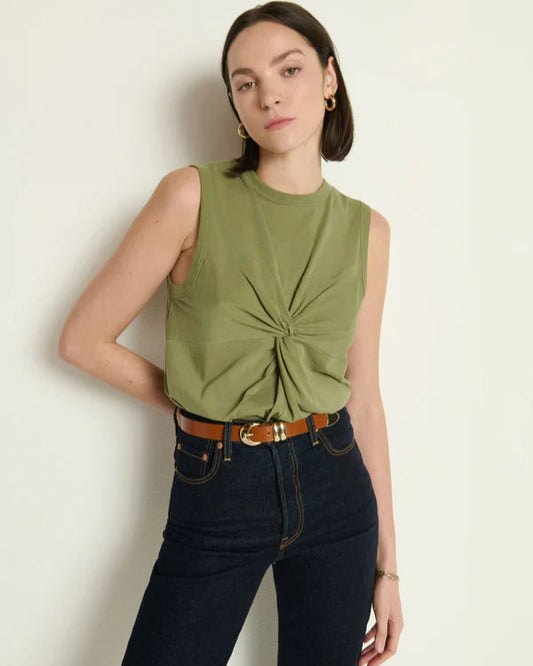 Woman wearing a green sleeveless top with a knot detail and dark jeans against a light background