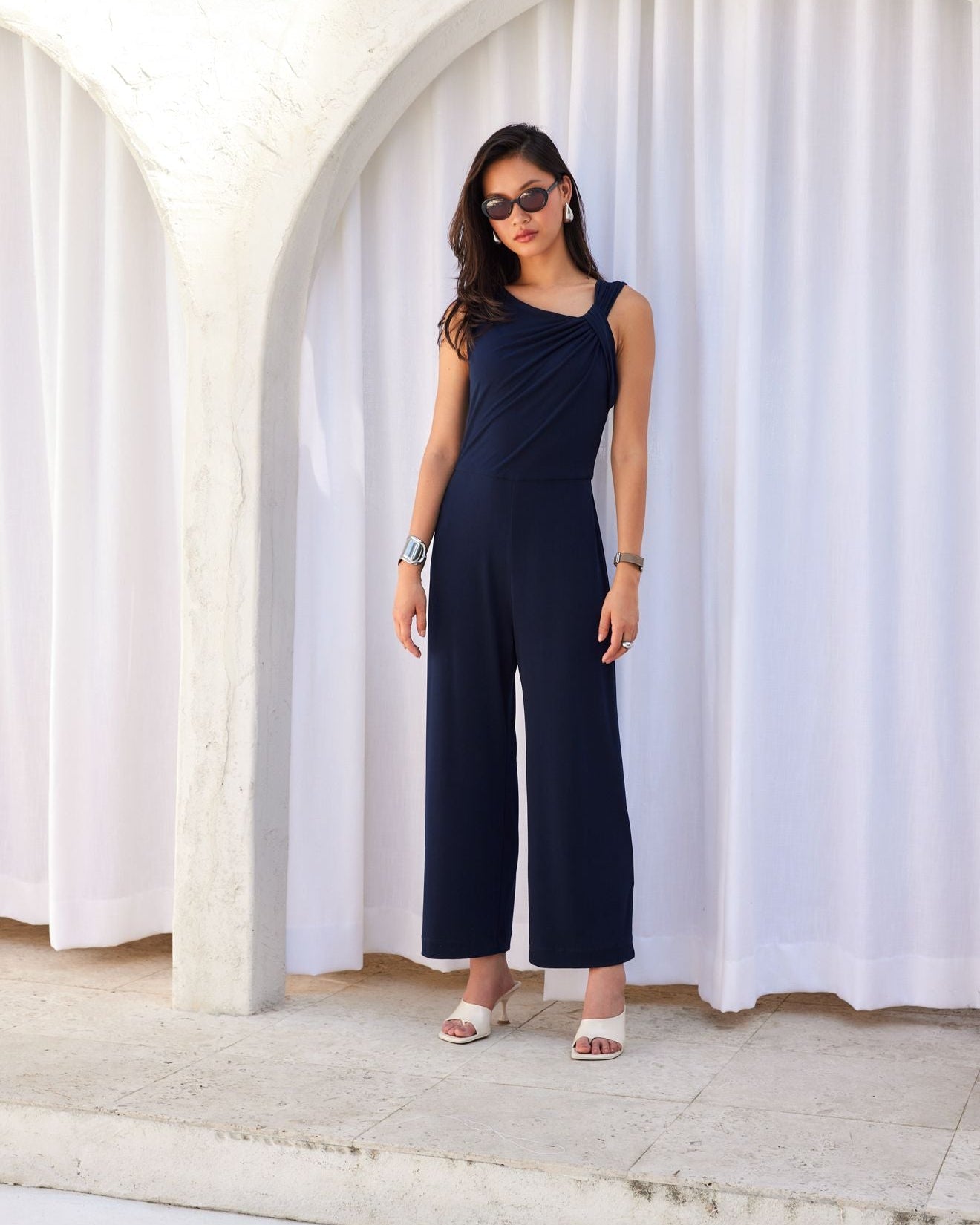 Woman wearing a navy jumpsuit standing in front of white curtains