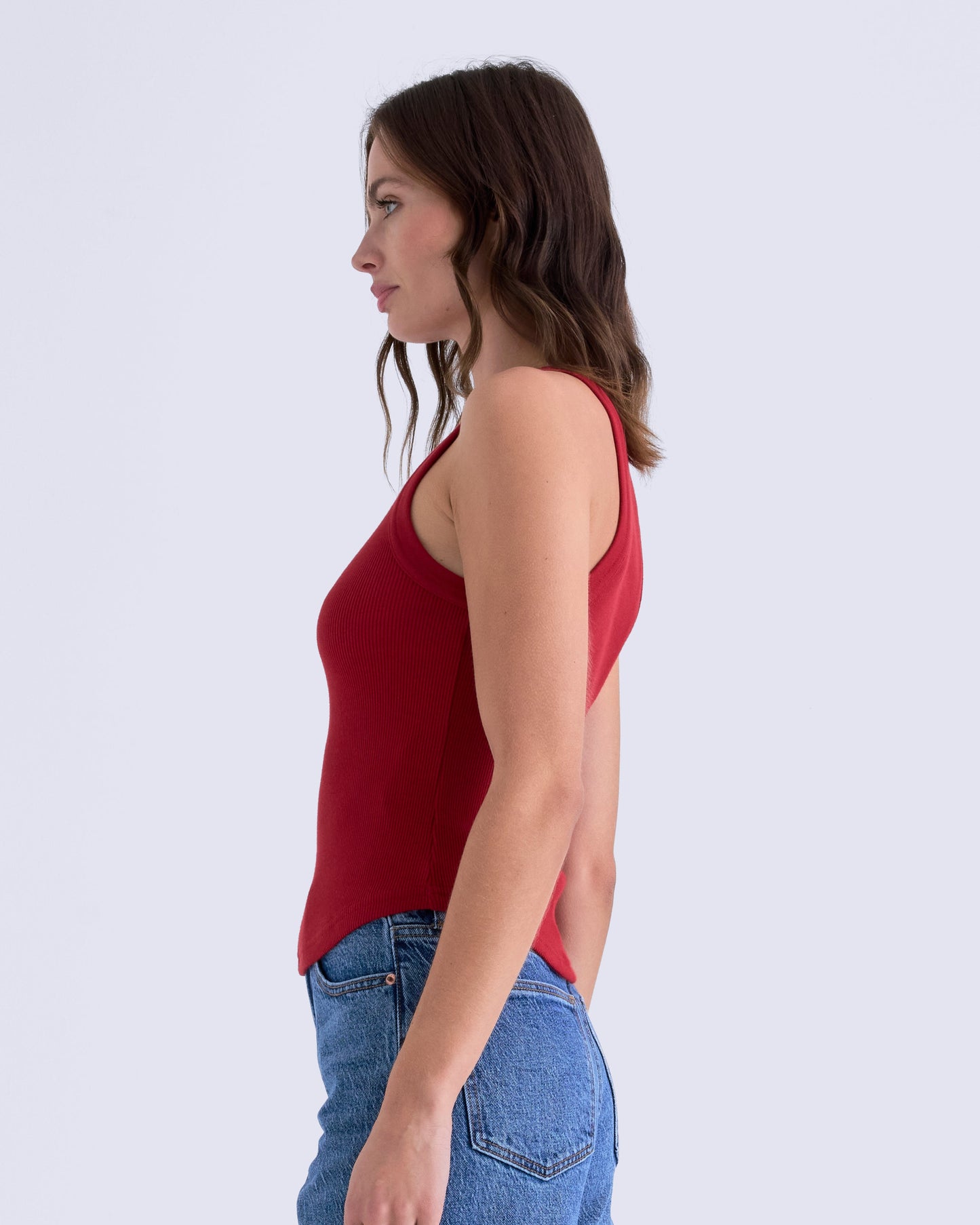 Woman wearing a red sleeveless top and blue jeans on a white background