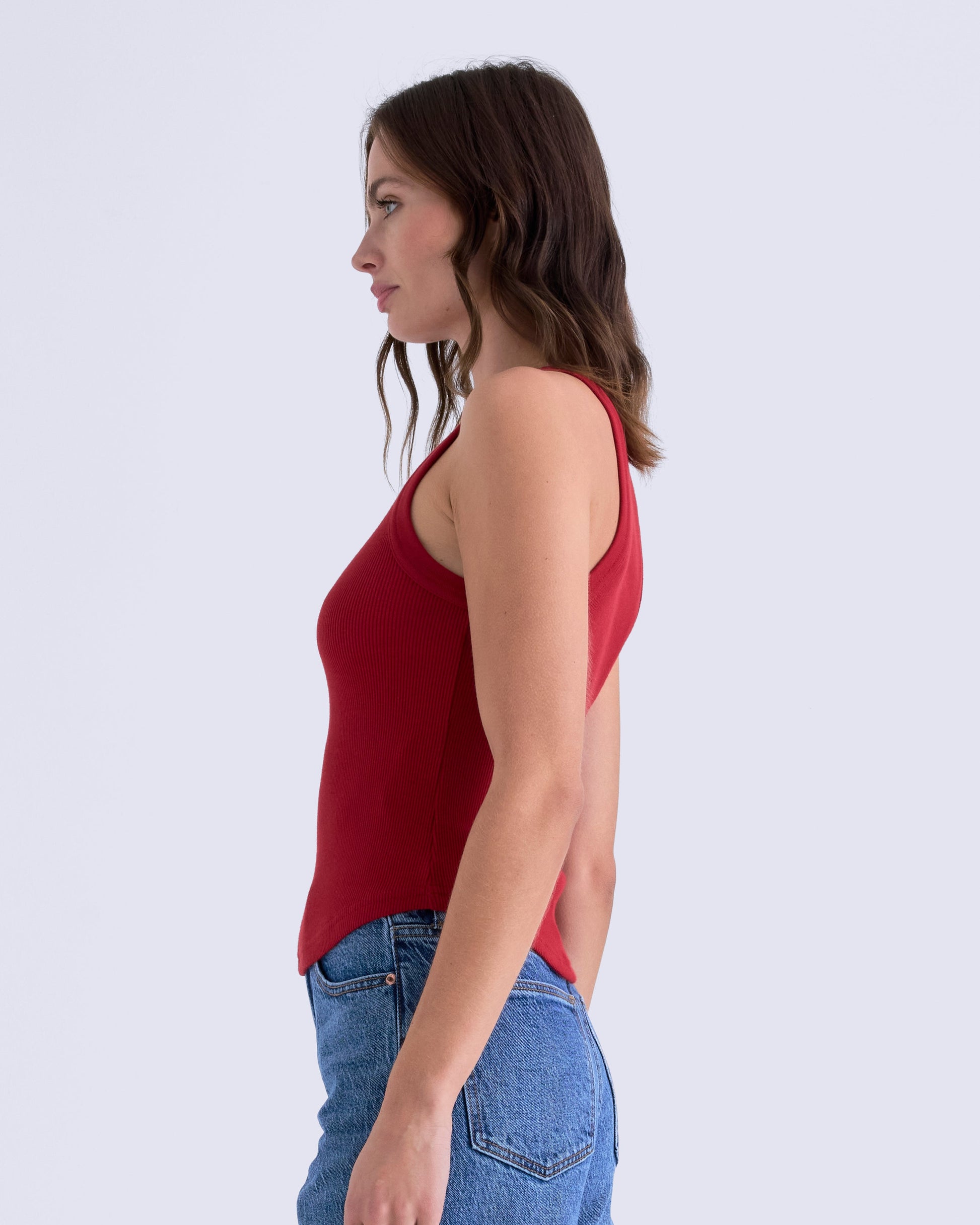 Woman wearing a red sleeveless top and blue jeans on a white background