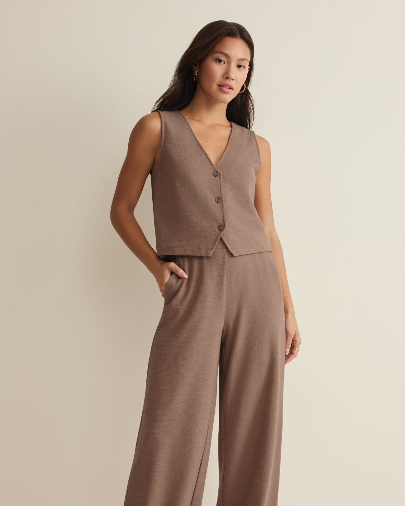 Woman wearing a brown vest and wide-leg pants on a beige background