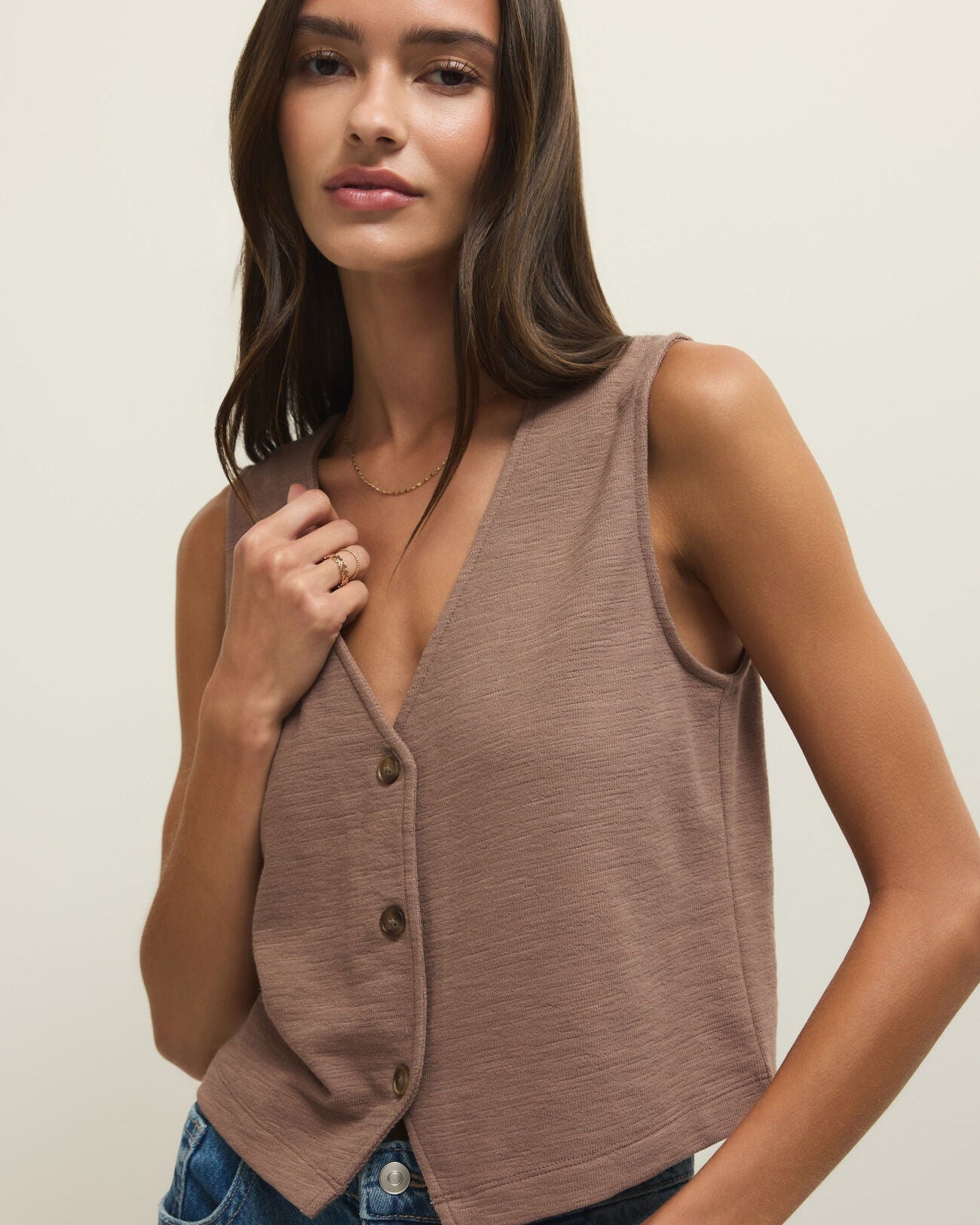 Woman wearing a brown sleeveless cardigan over a blue top against a plain background