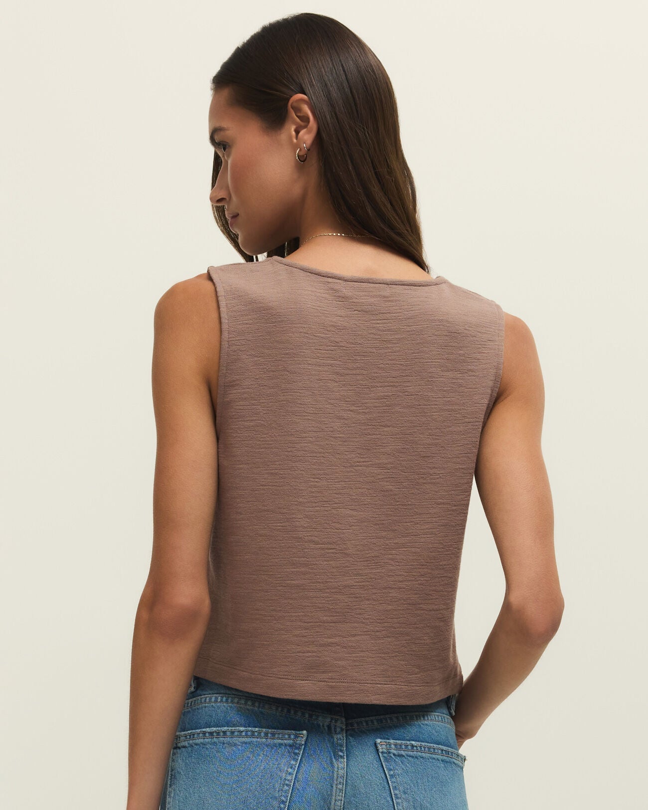 Woman wearing a brown sleeveless top and blue jeans on a beige background