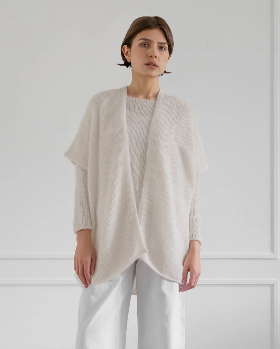 Woman wearing a light beige cardigan over a white top and pants against a plain background