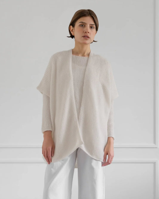 Woman wearing a light beige cardigan over a white top and pants against a plain background