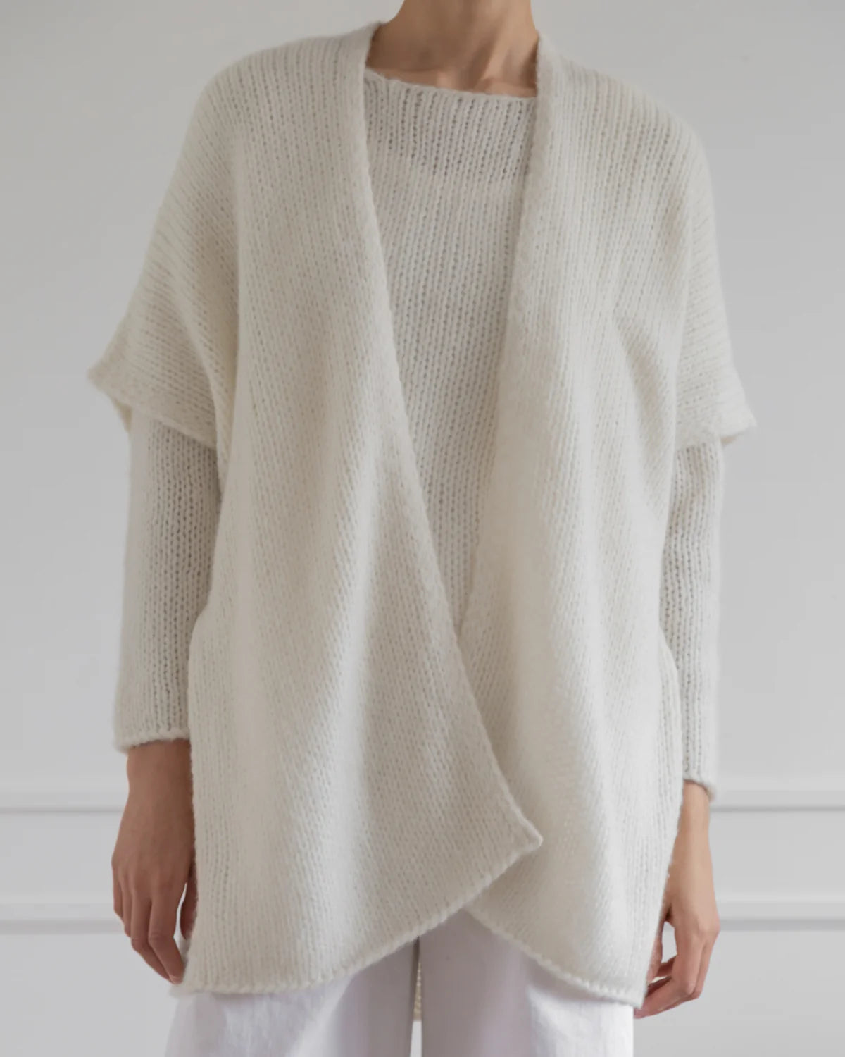 Person wearing a beige knitted cardigan against a white background