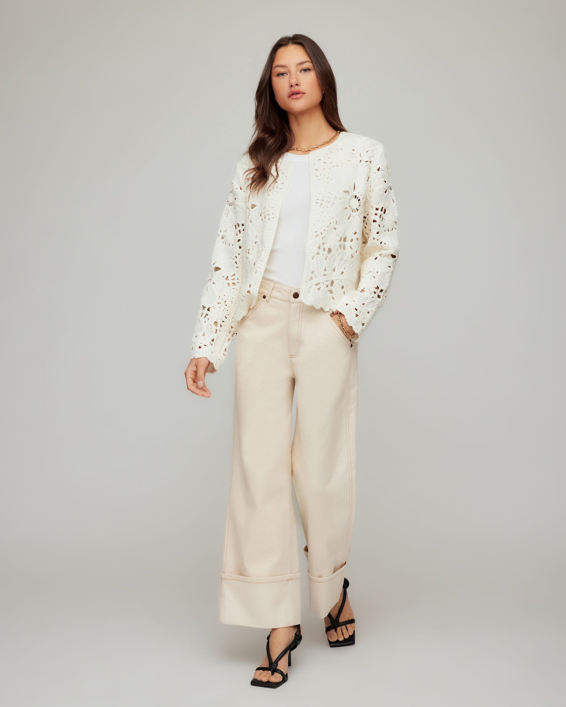 Woman wearing a white embroidered jacket and beige pants on a gray background