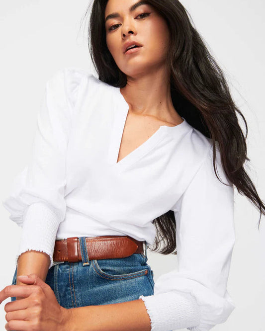 Woman wearing a white sweater and blue jeans with a brown belt on a white background