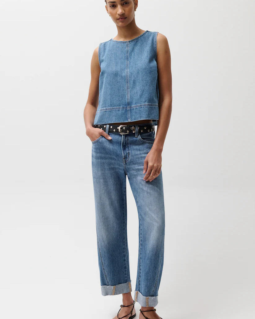 Model in denim top and jeans with a black belt in front of a white background
