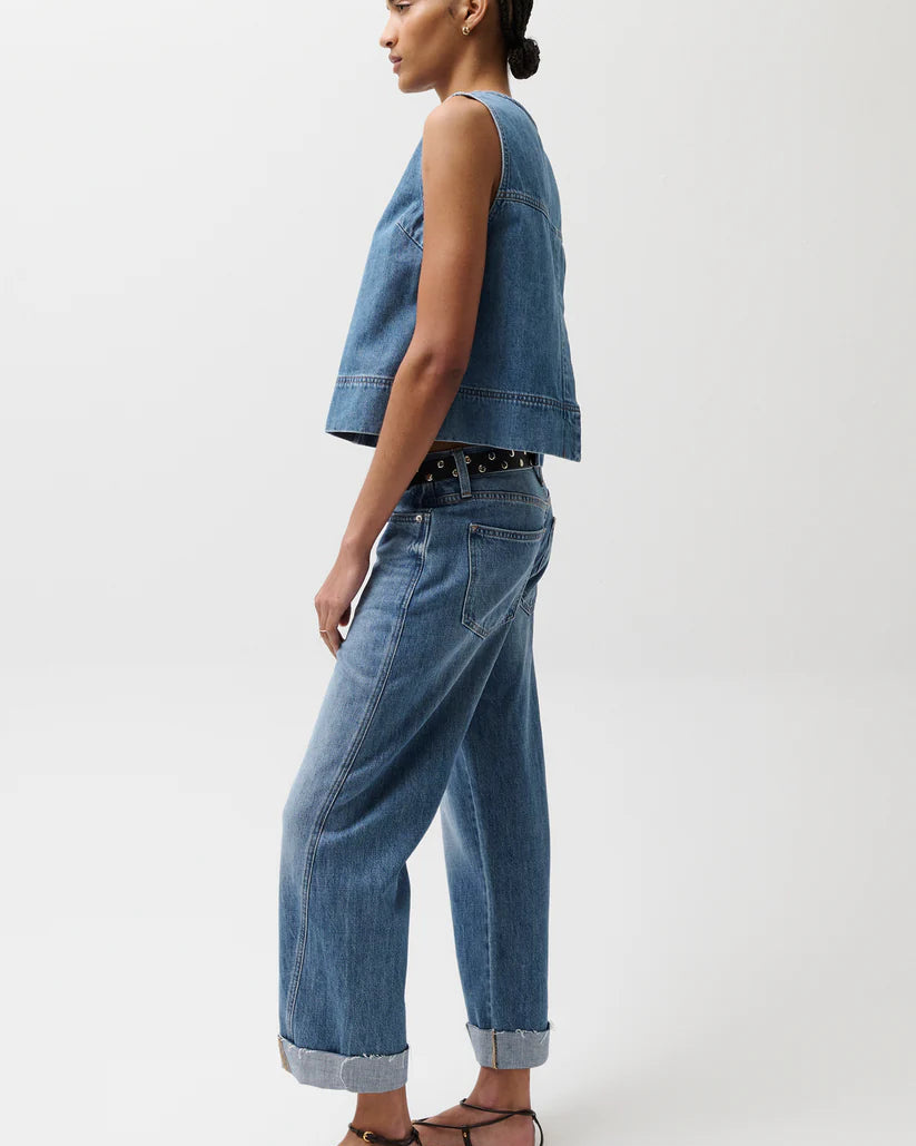 Model in a denim top with jeans and black strappy sandals in front of a white background.