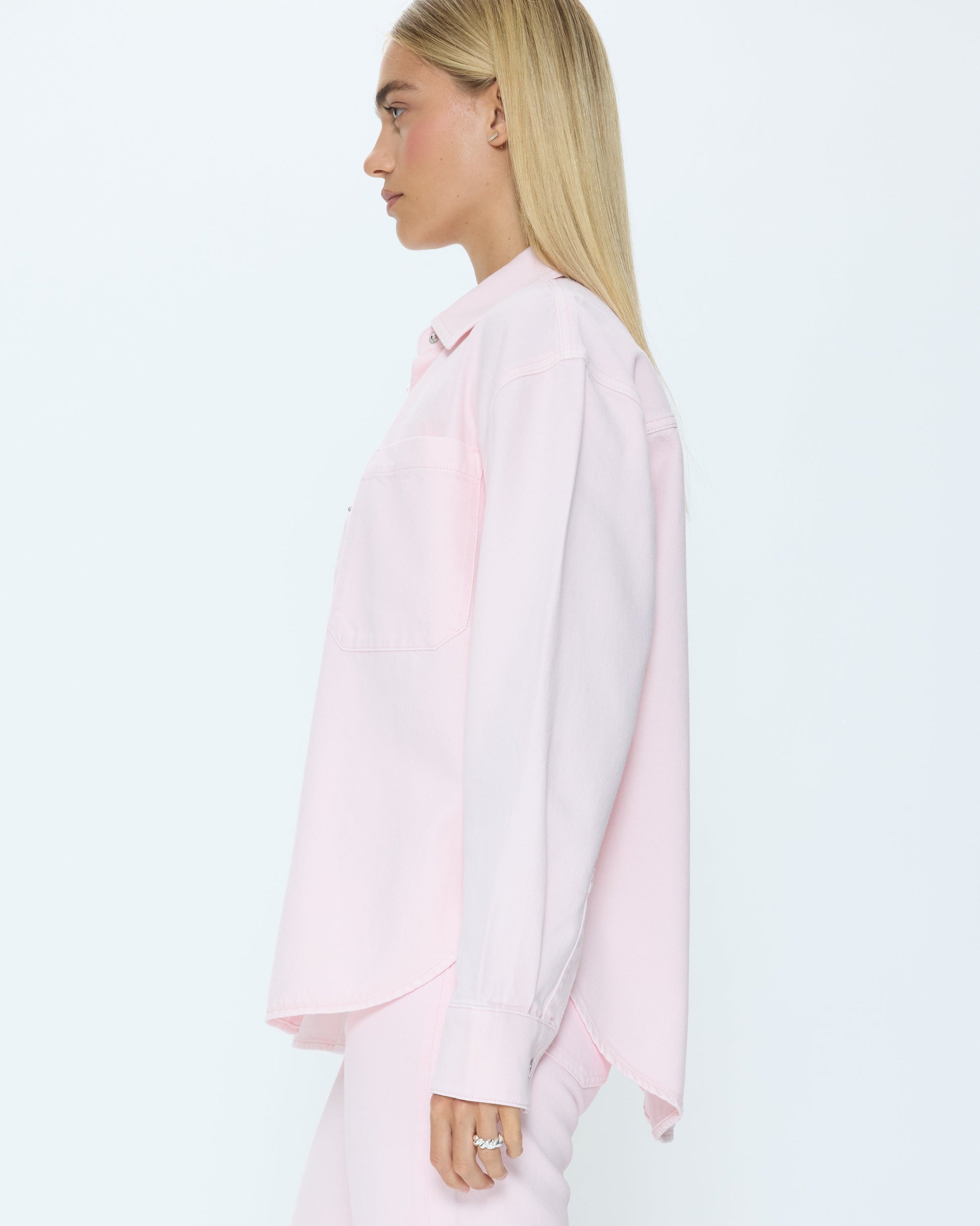 Woman wearing a light pink denim shirt and jeans on a white background