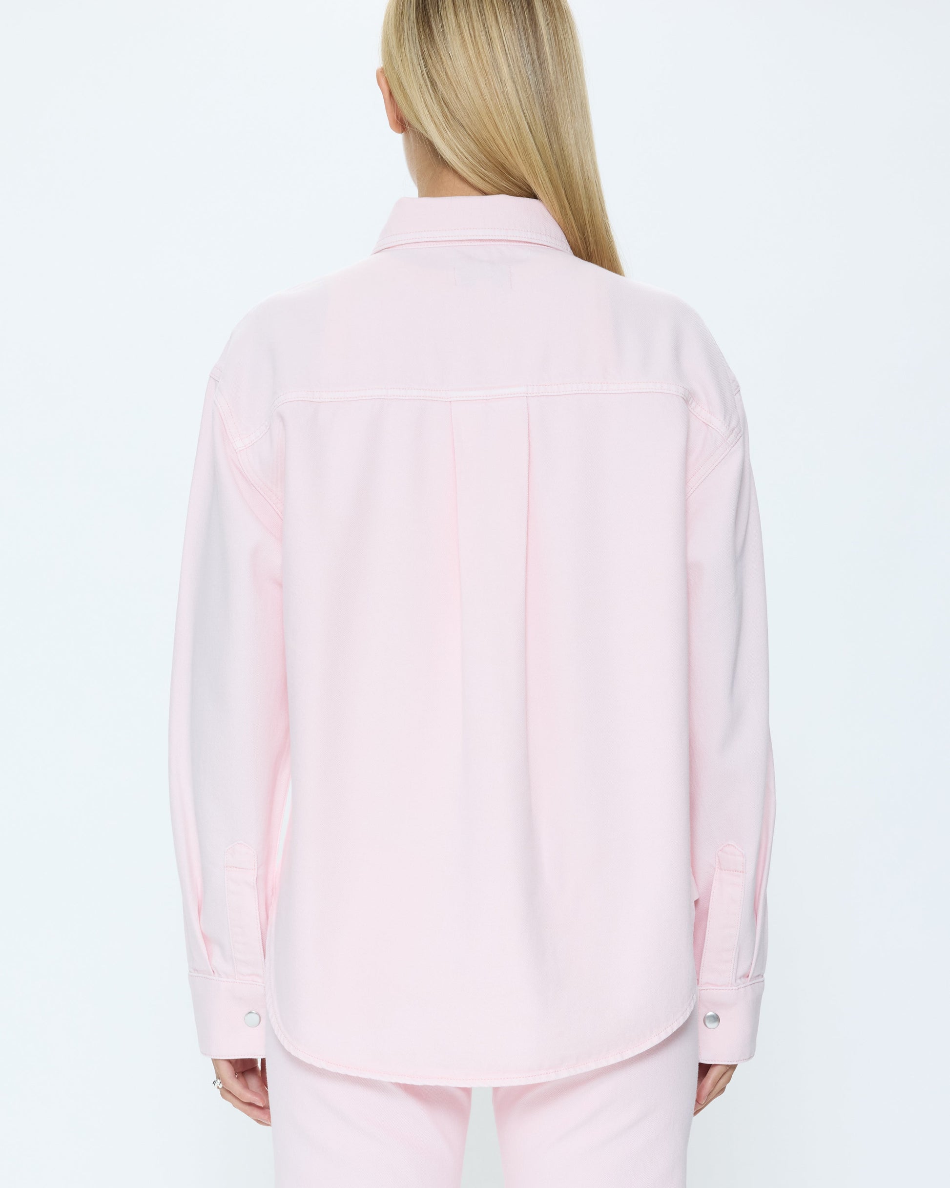Person wearing a light pink denim set on a white background