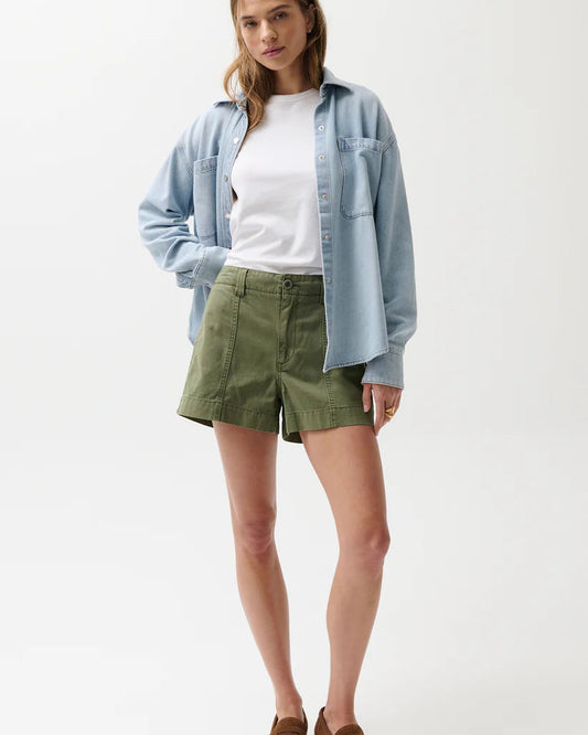 Woman wearing a light blue shirt, white top, green shorts, and brown shoes on a white background