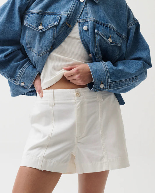 Person wearing a blue denim jacket and white shorts on a plain background