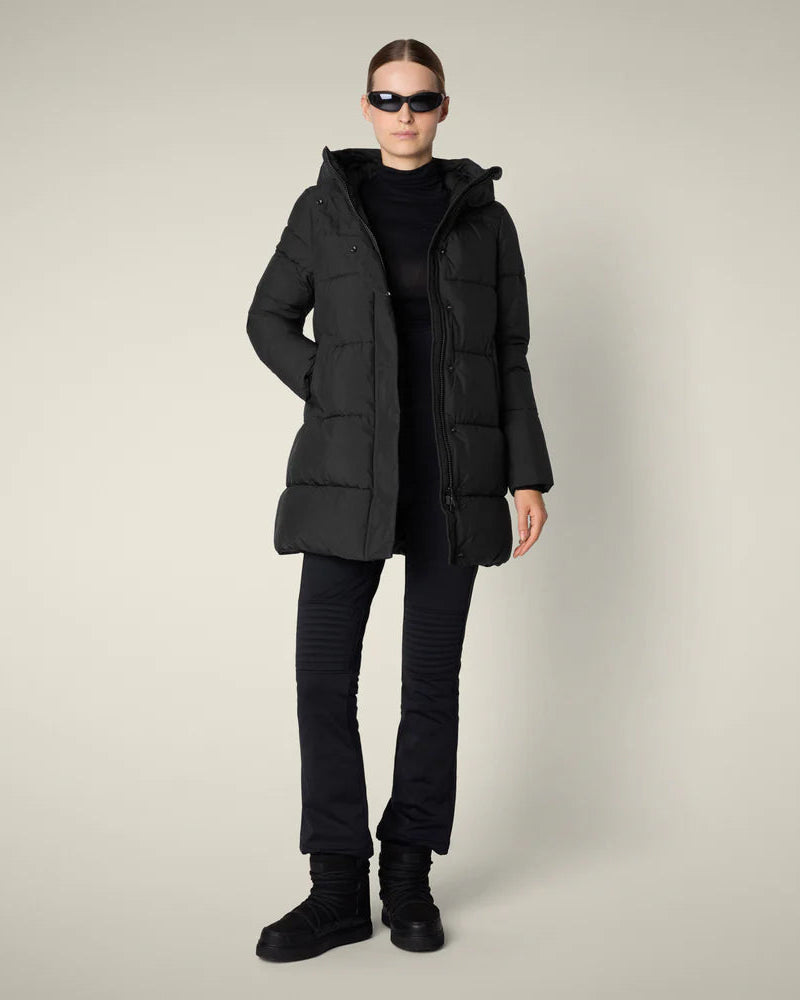 Woman wearing black puffer with black pants against plain ground.