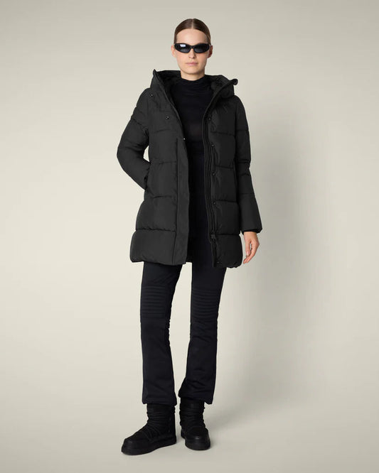 Woman wearing black puffer with black pants against plain ground.