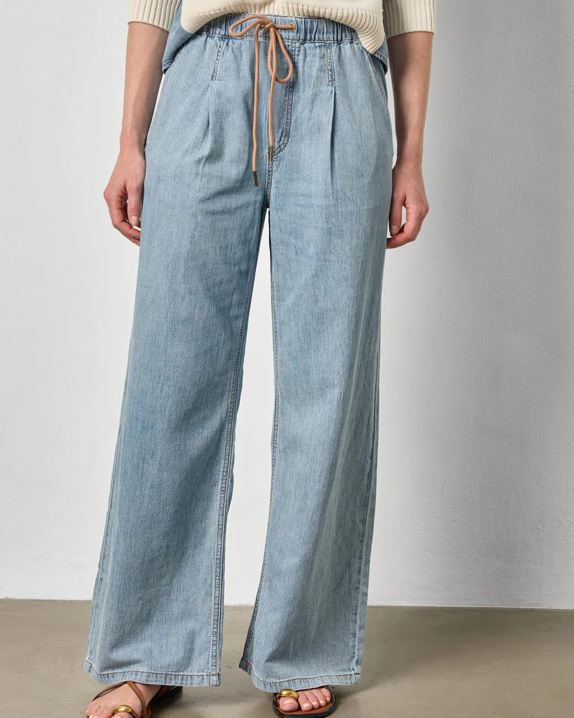 Person wearing light blue wide-leg jeans and a beige sweater against a plain background