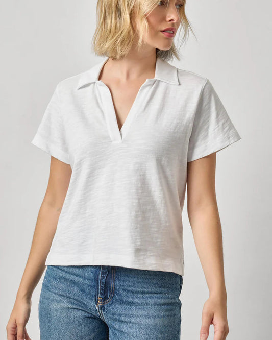 Woman wearing a white polo shirt and blue jeans against a plain background