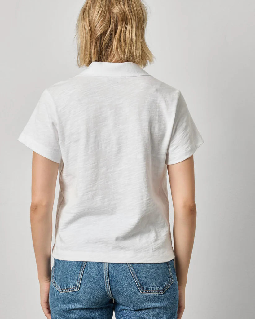 Person wearing a white polo shirt and blue jeans on a plain background