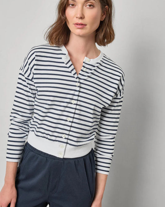 Woman wearing a striped shirt and navy pants against a plain background