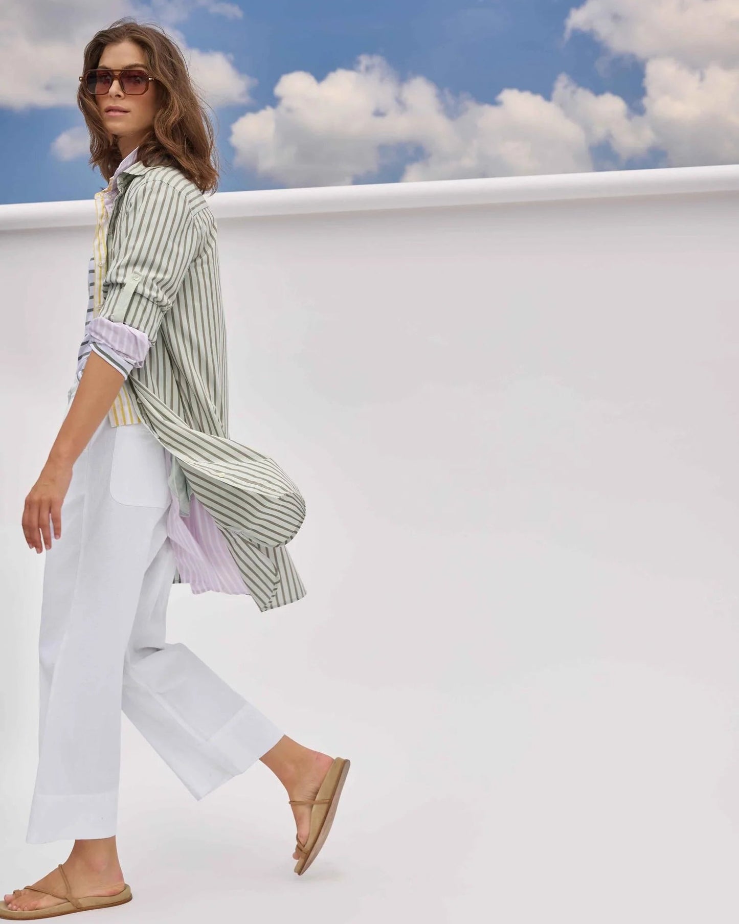 Woman wearing a striped shirt and white pants against a blue sky with clouds.