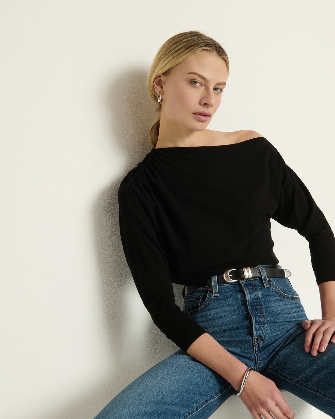 Model wearing the Nation Pietra top in Jet Black with blue jeans sitting in front of a white background