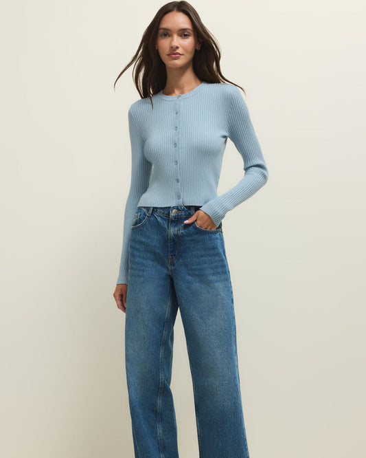 Woman wearing a light blue cardigan and blue jeans on a plain background