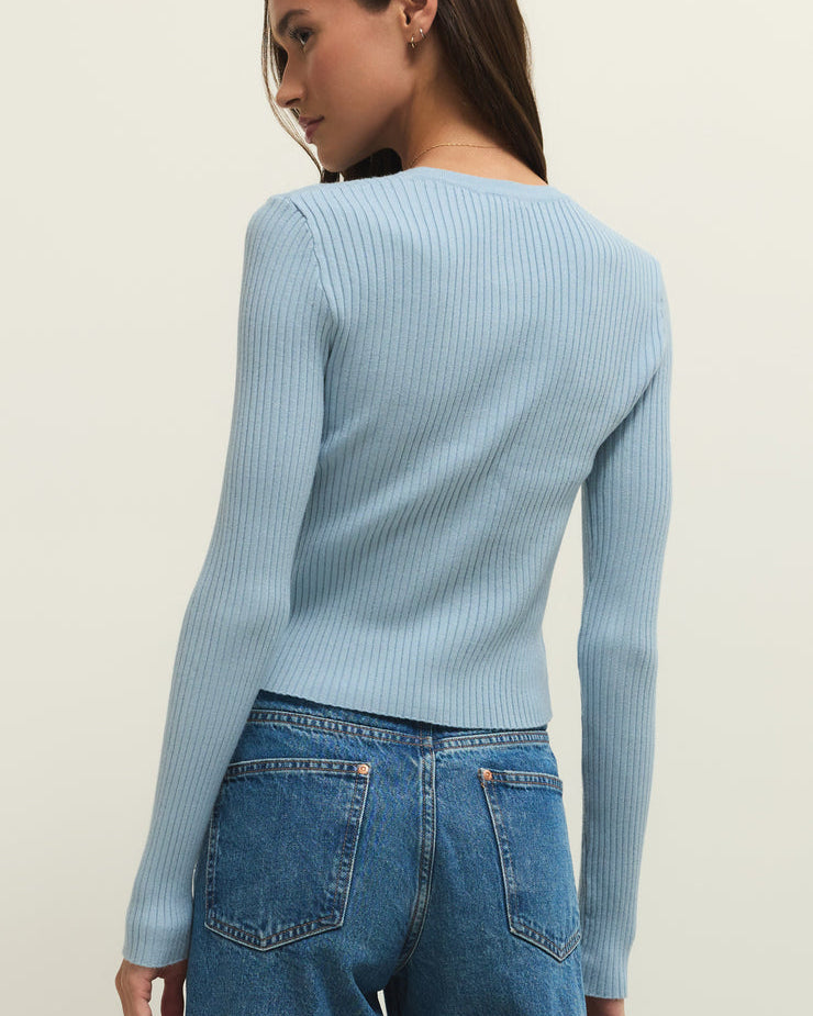 Woman wearing a light blue ribbed sweater and blue jeans on a beige background