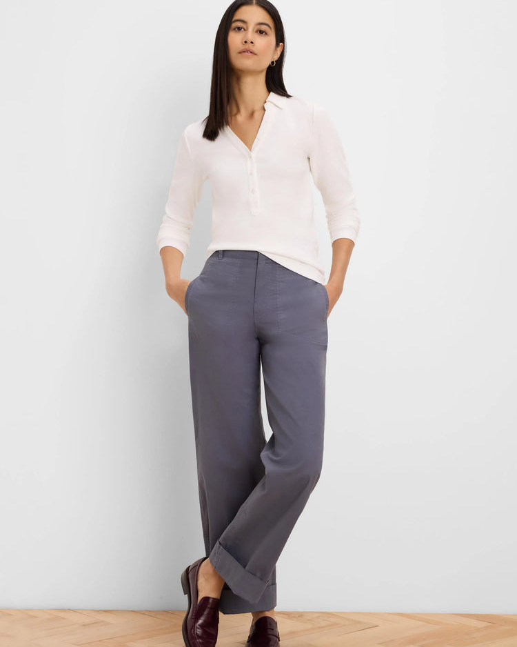 A woman modeling a white long-sleeve button-up shirt and gray wide-leg trousers, paired with dark brown loafers, standing against a light gray wall on a light wood floor.