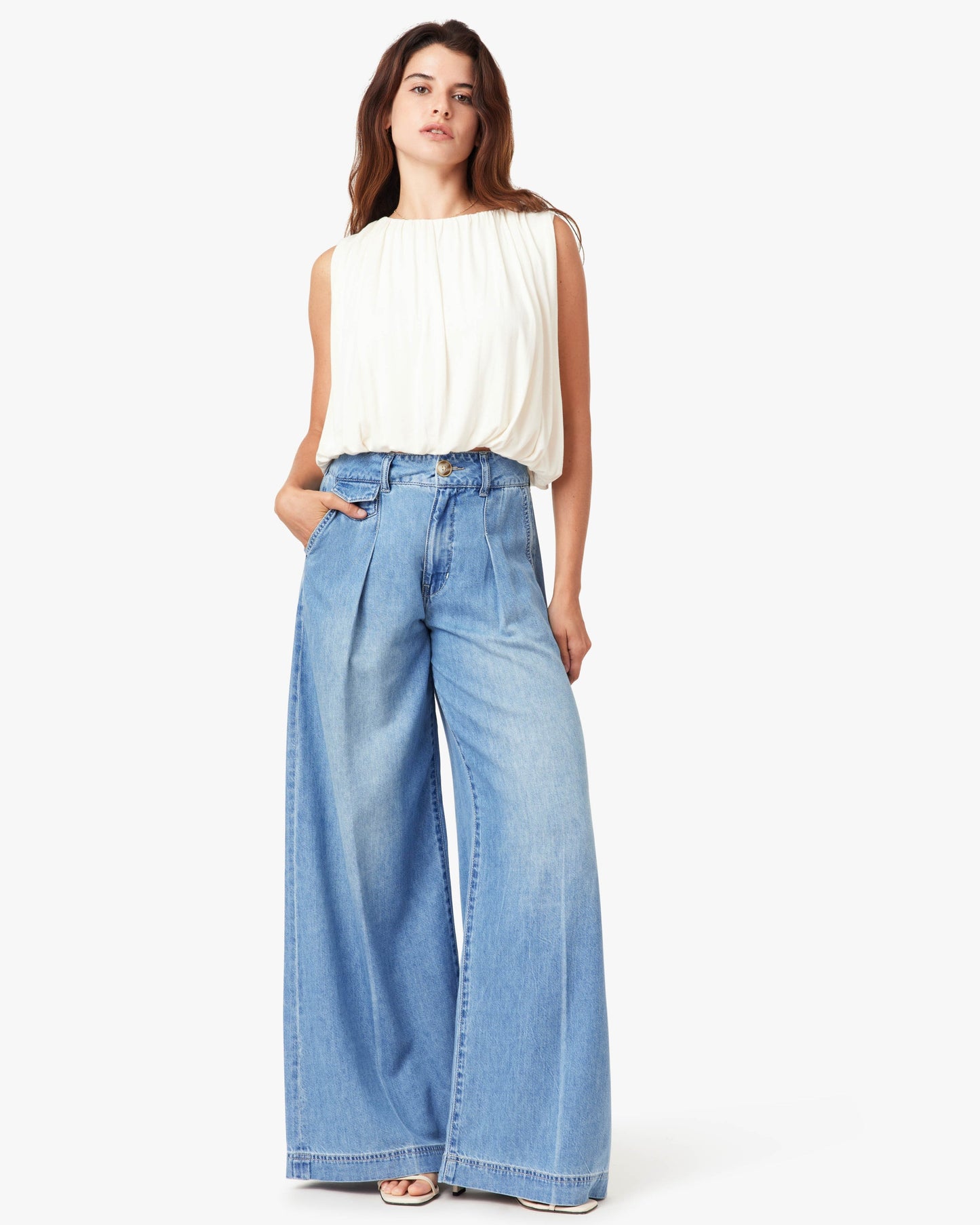 Woman wearing a white sleeveless top and light blue wide-leg jeans on a white background