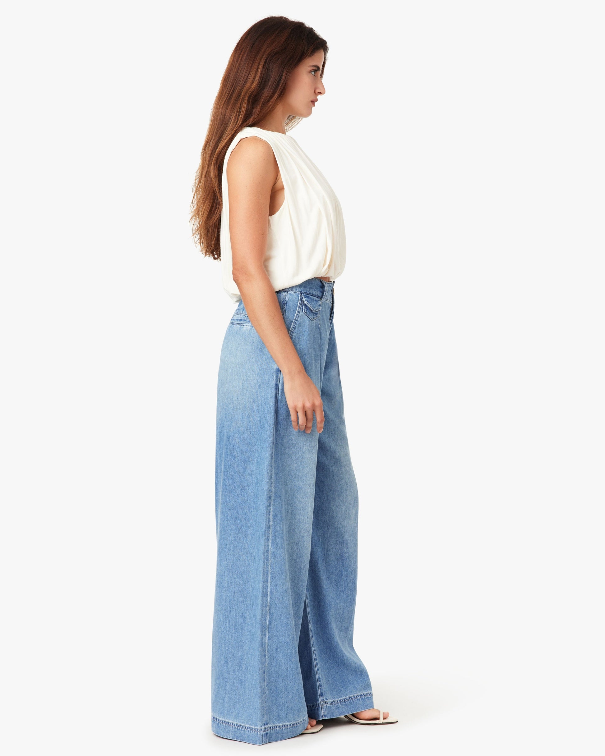 Woman wearing a white sleeveless top and blue wide-leg jeans on a white background