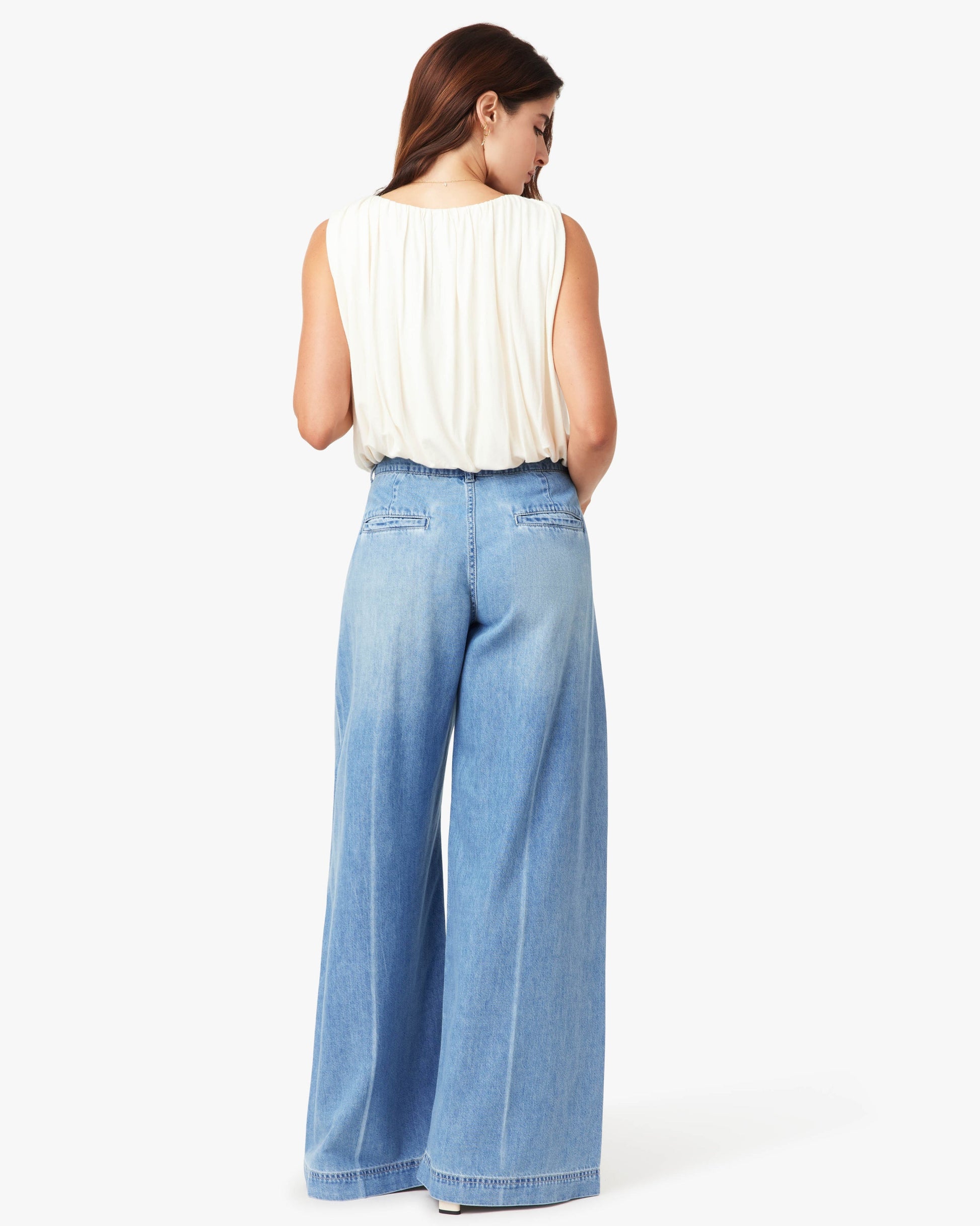 Woman wearing a white sleeveless top and light blue wide-leg jeans on a white background