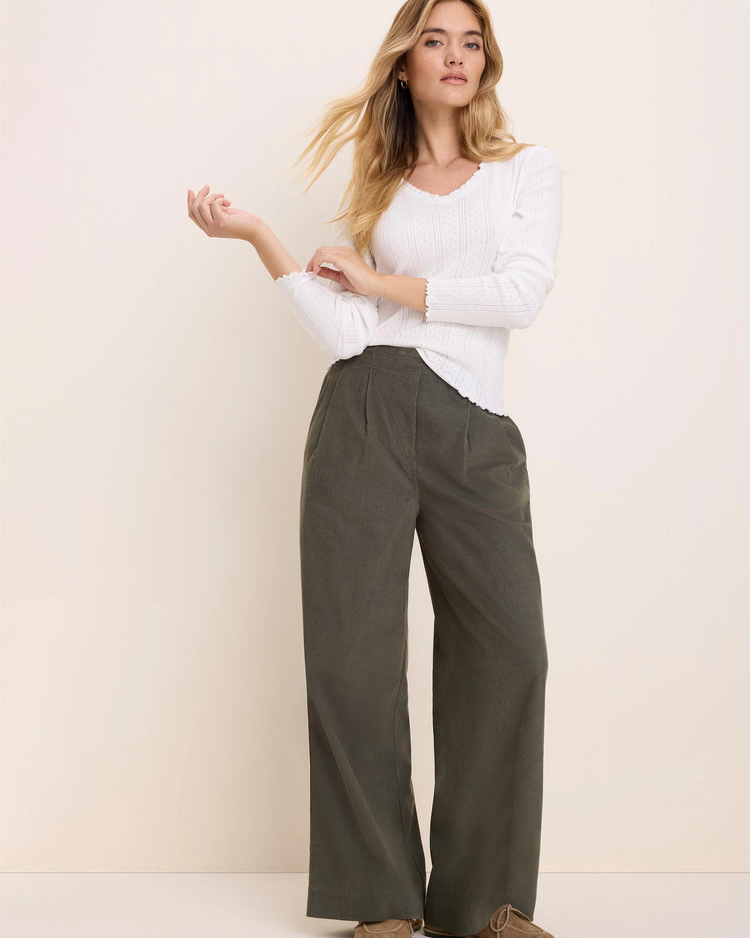 A woman modeling a white long-sleeve top and olive green wide-leg trousers against a plain beige studio background.