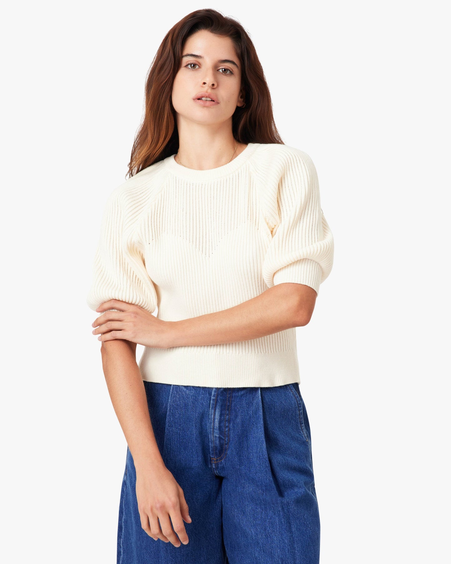 Woman wearing a white sweater and blue pants on a white background