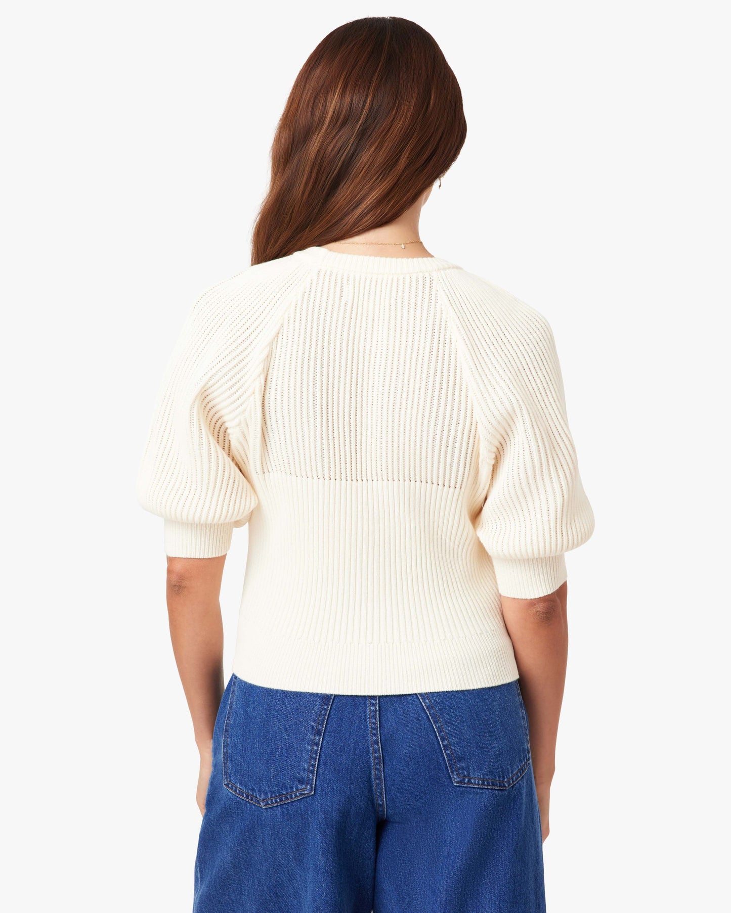 Person wearing a cream sweater and blue jeans on a white background