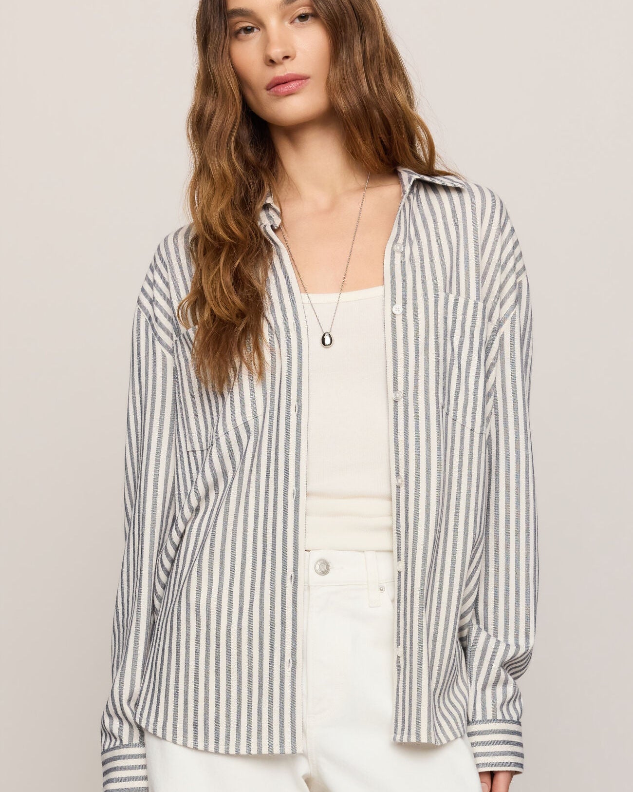Woman wearing a striped shirt over a white top with a neutral background