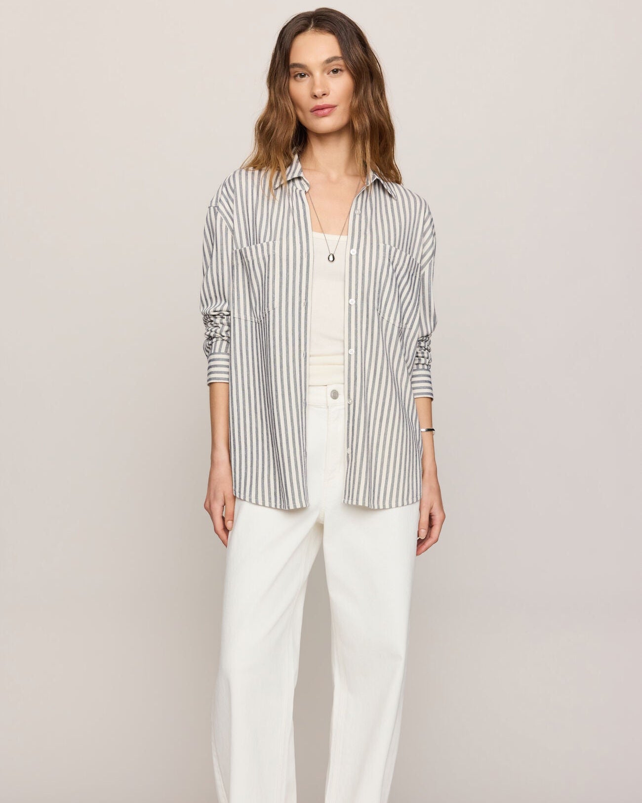 Woman wearing a striped shirt and white pants on a plain background