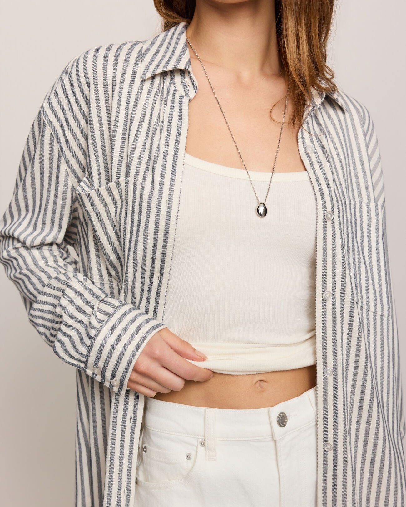 Person wearing a striped shirt over a white top and pants on a plain background