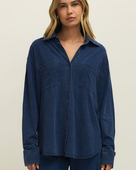 Woman wearing a blue shirt and pants against a beige background