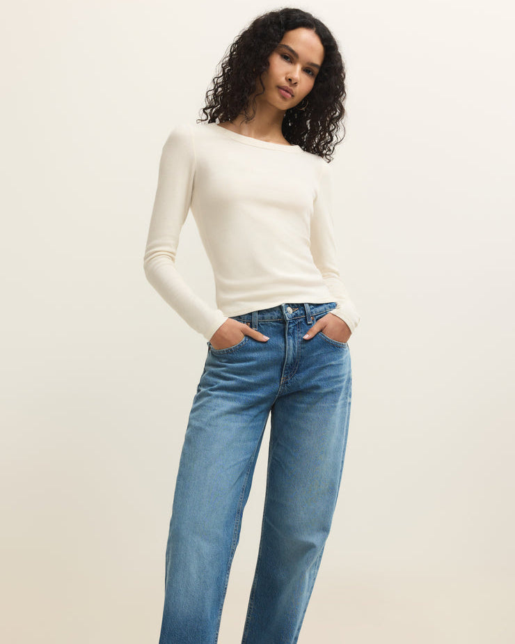 Woman wearing a white sweater and blue jeans against a plain background