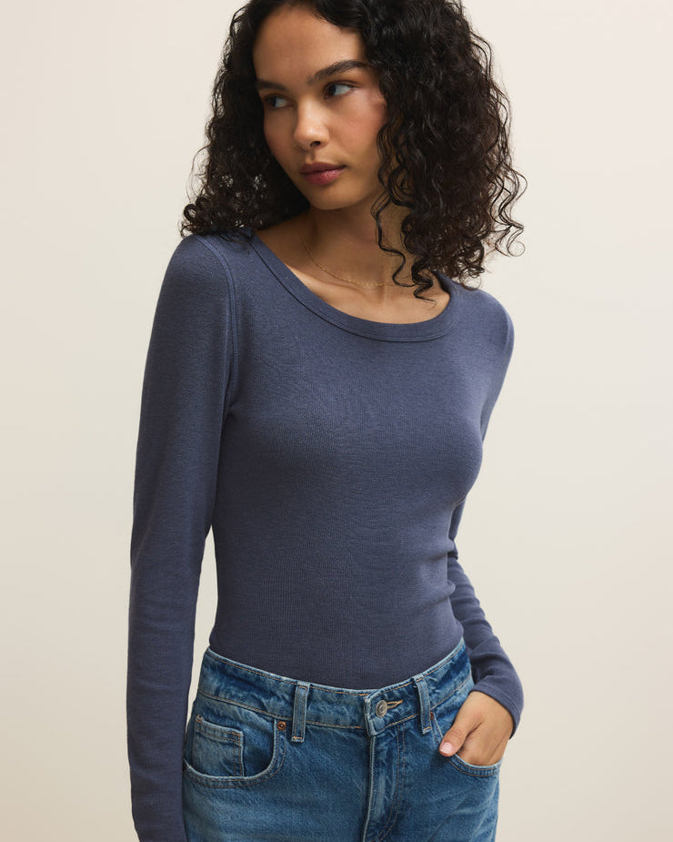 Woman wearing a blue long-sleeve top and jeans against a plain background
